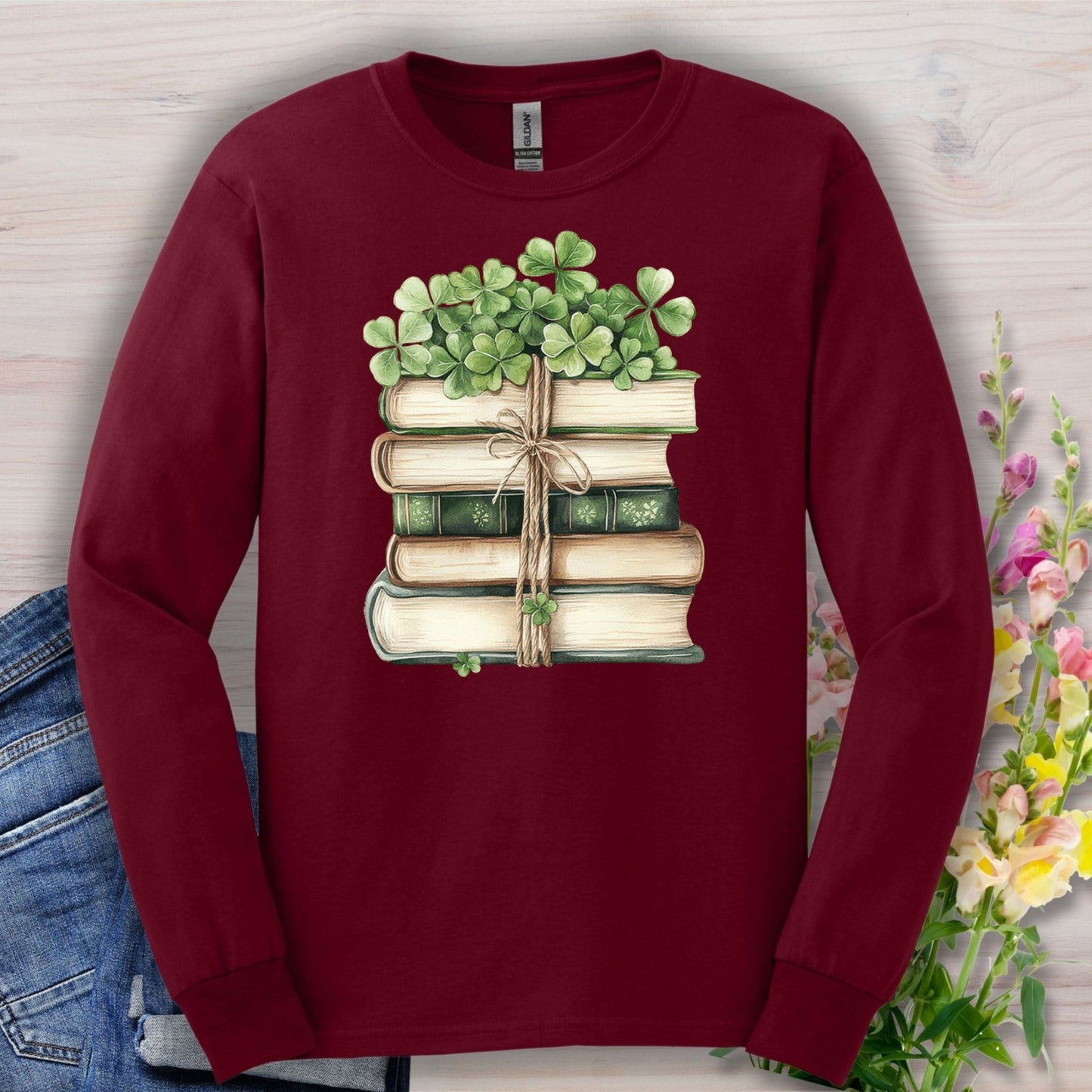 Maroon long sleeve tee with a watercolor stack of vintage books tied with twine and clovers.