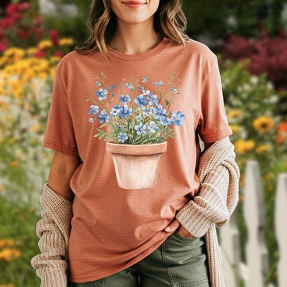 Garment-dyed terracotta t-shirt with a watercolor pot of blue forget-me-nots, worn by a woman.
