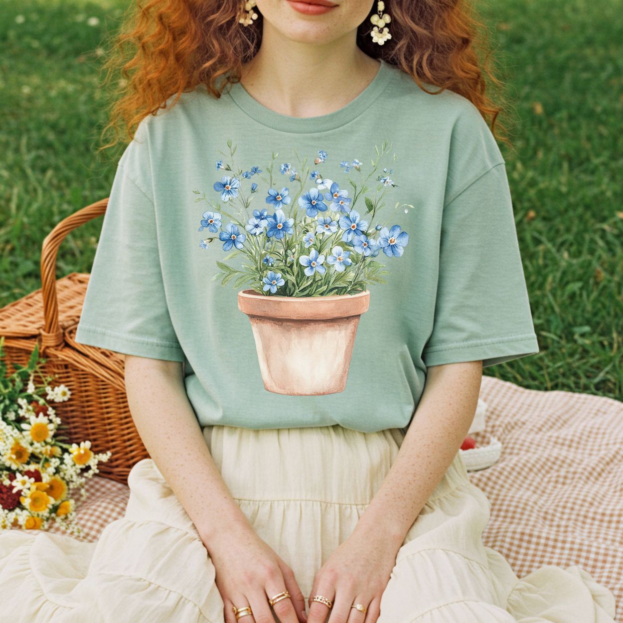 Garment-dyed sage green t-shirt with a watercolor terracotta pot of blue forget-me-nots.