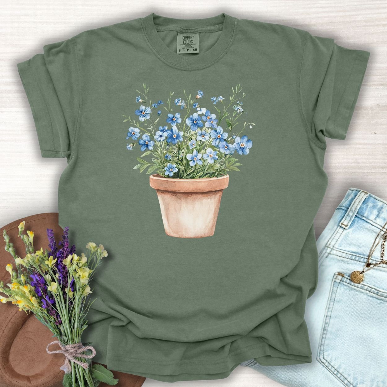 Moss green relaxed-fit t-shirt with a watercolor terracotta pot of blue forget-me-nots.