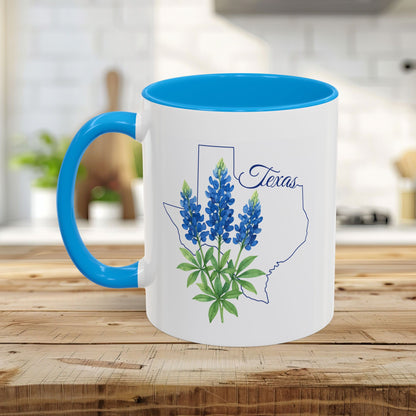White ceramic mug with blue interior and handle, featuring a Texas outline and bluebonnet flowers.