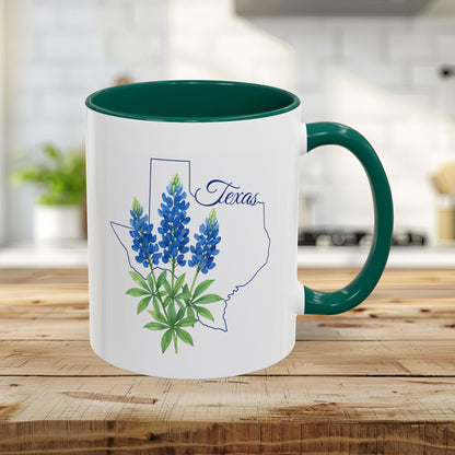 White 11oz ceramic mug with green interior and handle, featuring a bluebonnet illustration inside a Texas outline.