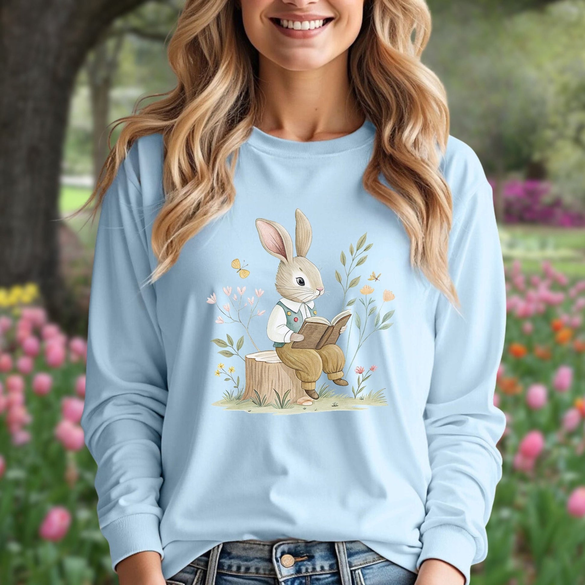 Light blue long sleeve tee with a whimsical rabbit reading on a tree stump, surrounded by flowers and butterflies.
