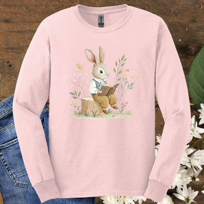 Light pink long-sleeve tee with a watercolor rabbit reading on a stump, surrounded by botanicals.