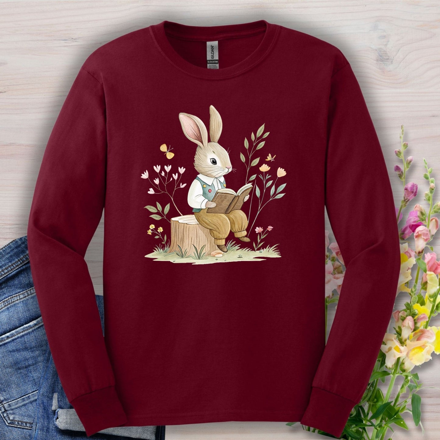 Maroon long-sleeve tee with a whimsical rabbit reading on a tree stump, surrounded by botanical elements.