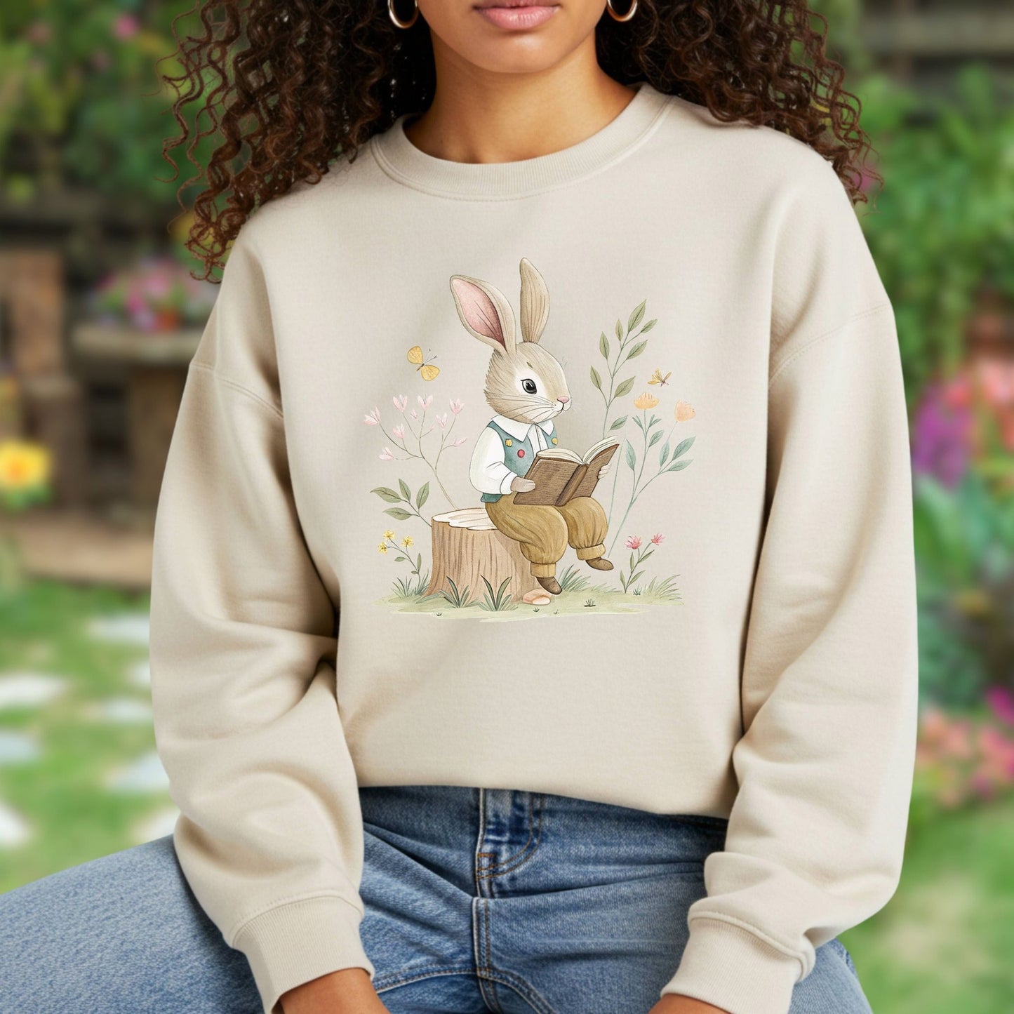 Beige sweatshirt with a charming bunny in a waistcoat reading on a tree stump, surrounded by flowers.