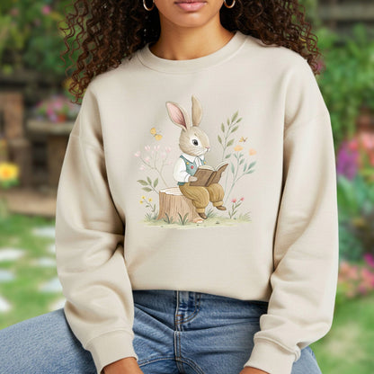 Beige sweatshirt with a charming bunny in a waistcoat reading on a tree stump, surrounded by flowers.