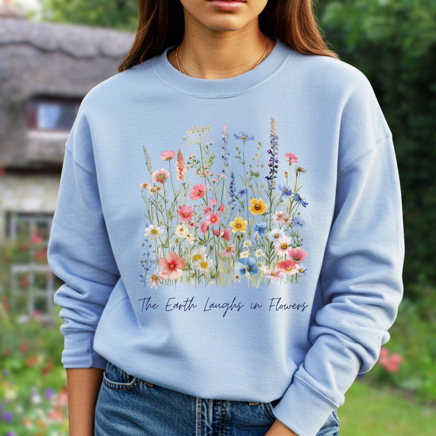 Light blue crewneck sweatshirt with a colorful wildflower bouquet print and "The Earth Laughs in Flowers" text.