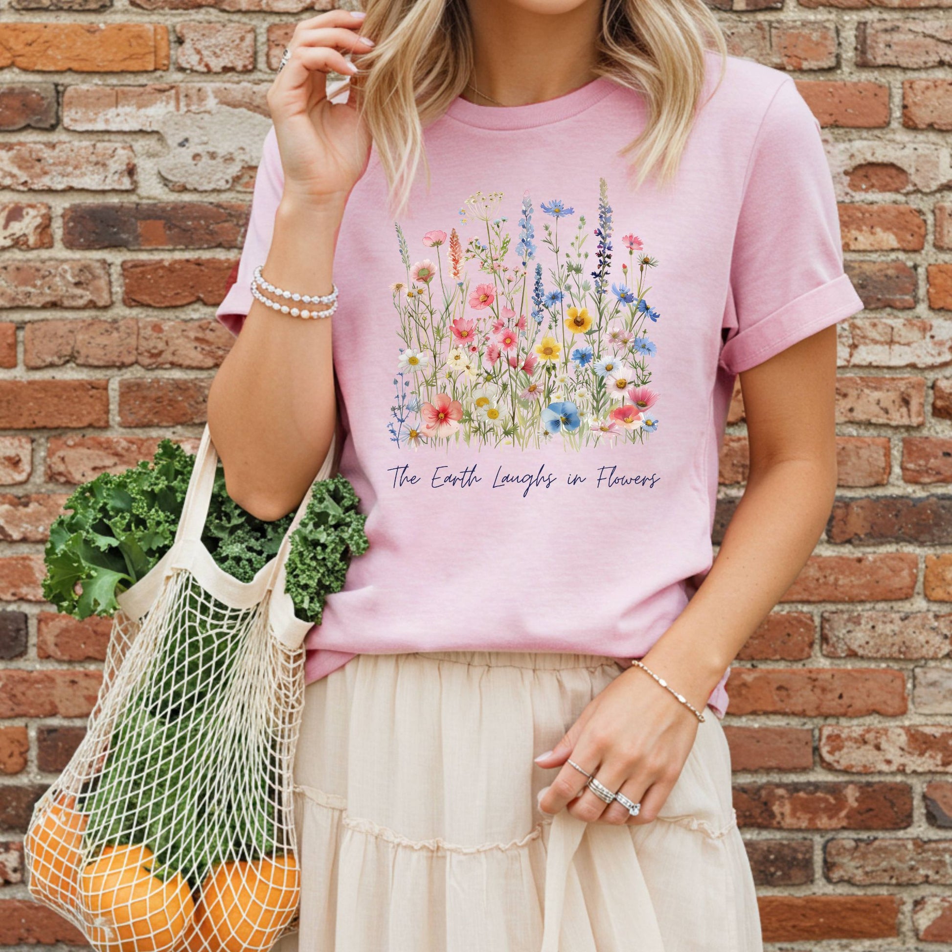 Garment-dyed pink t-shirt with painterly wildflowers and "The Earth Laughs in Flowers" text.