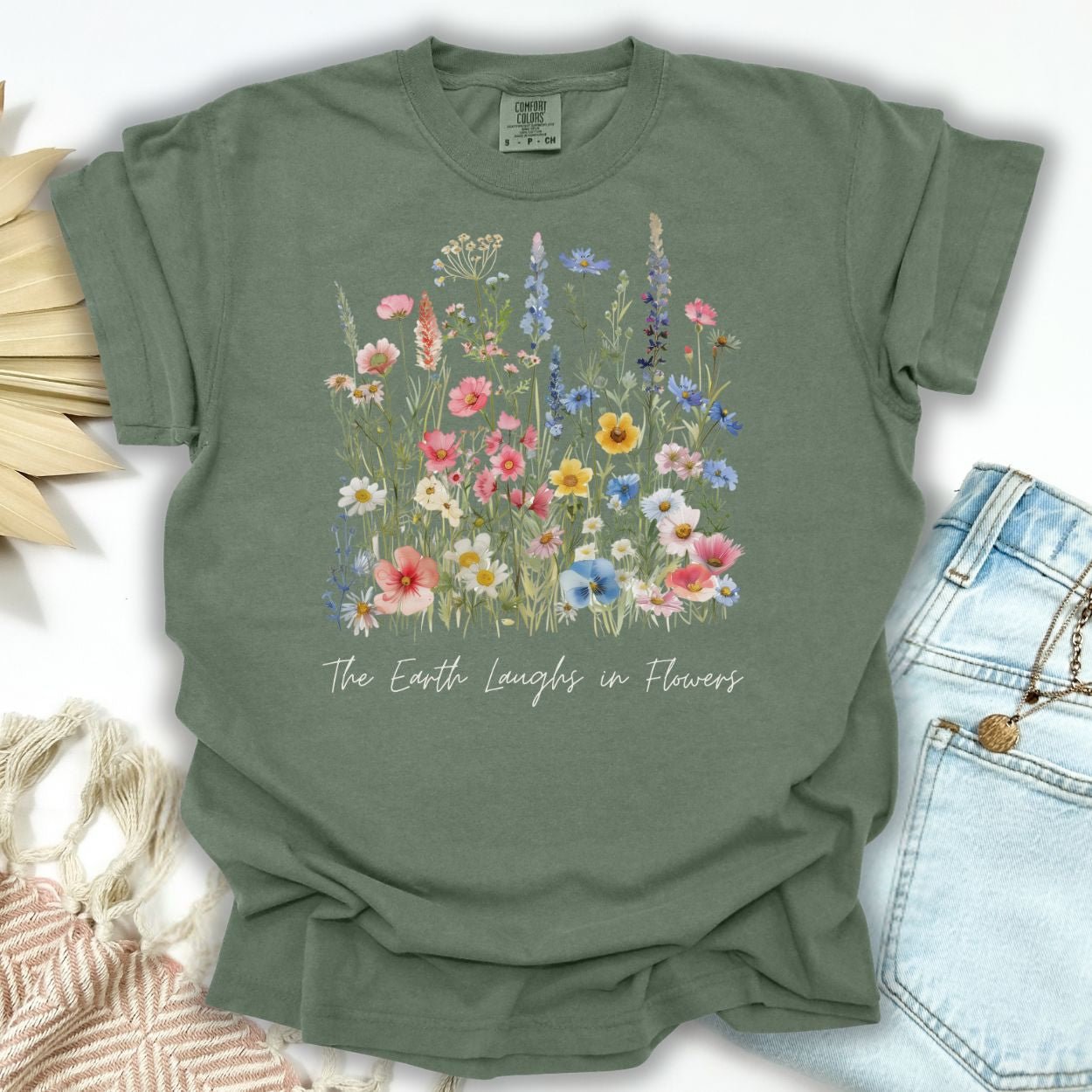 Moss green garment-dyed t-shirt with painterly wildflowers and "The Earth Laughs in Flowers" text.