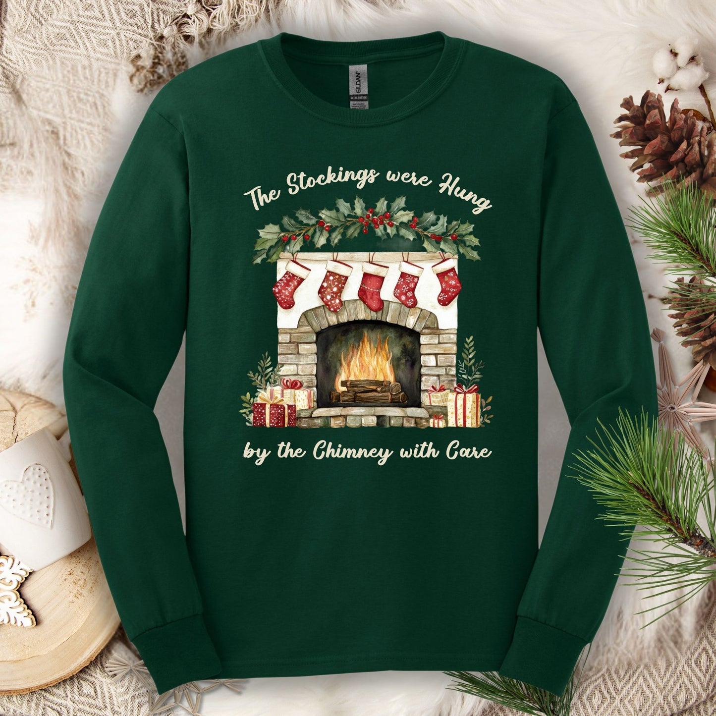 Forest Green long sleeve tee with a watercolor fireplace, red stockings, holly, and "The Stockings were Hung" text.