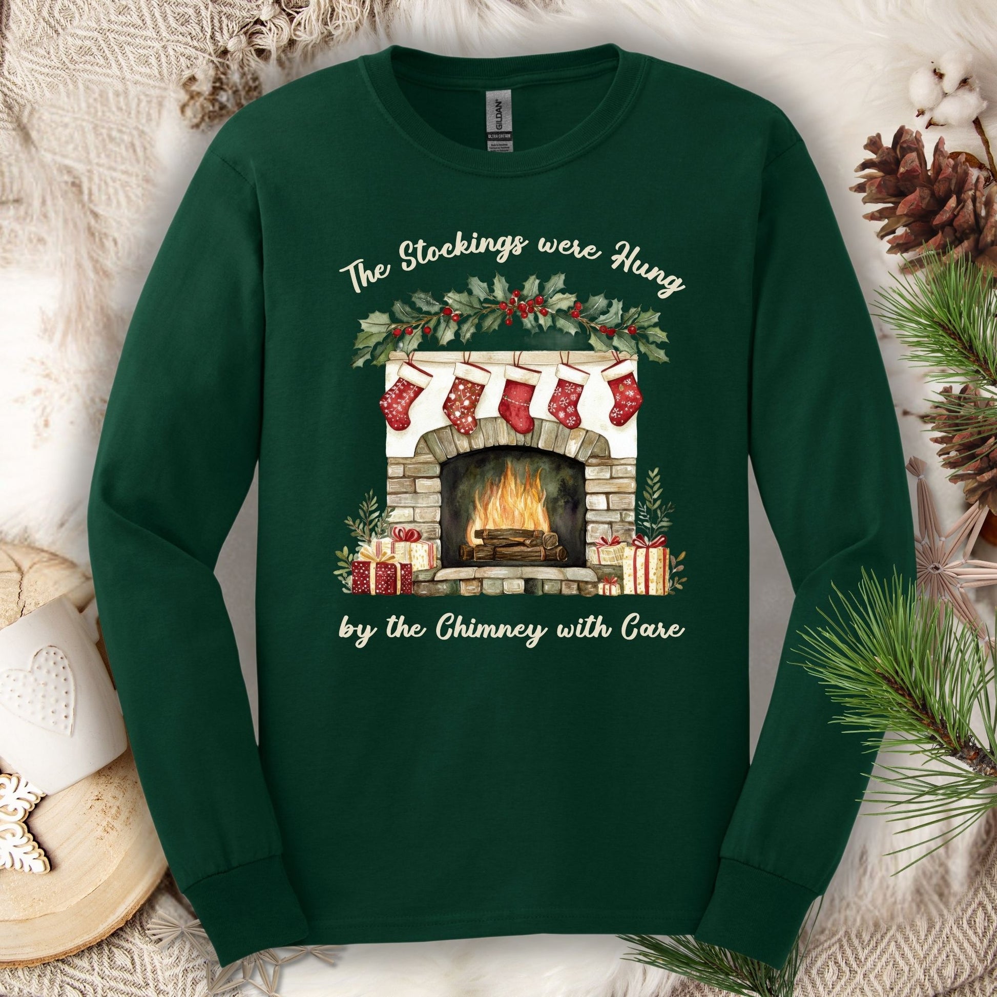 Forest Green long sleeve tee with a watercolor fireplace, red stockings, holly, and "The Stockings were Hung" text.