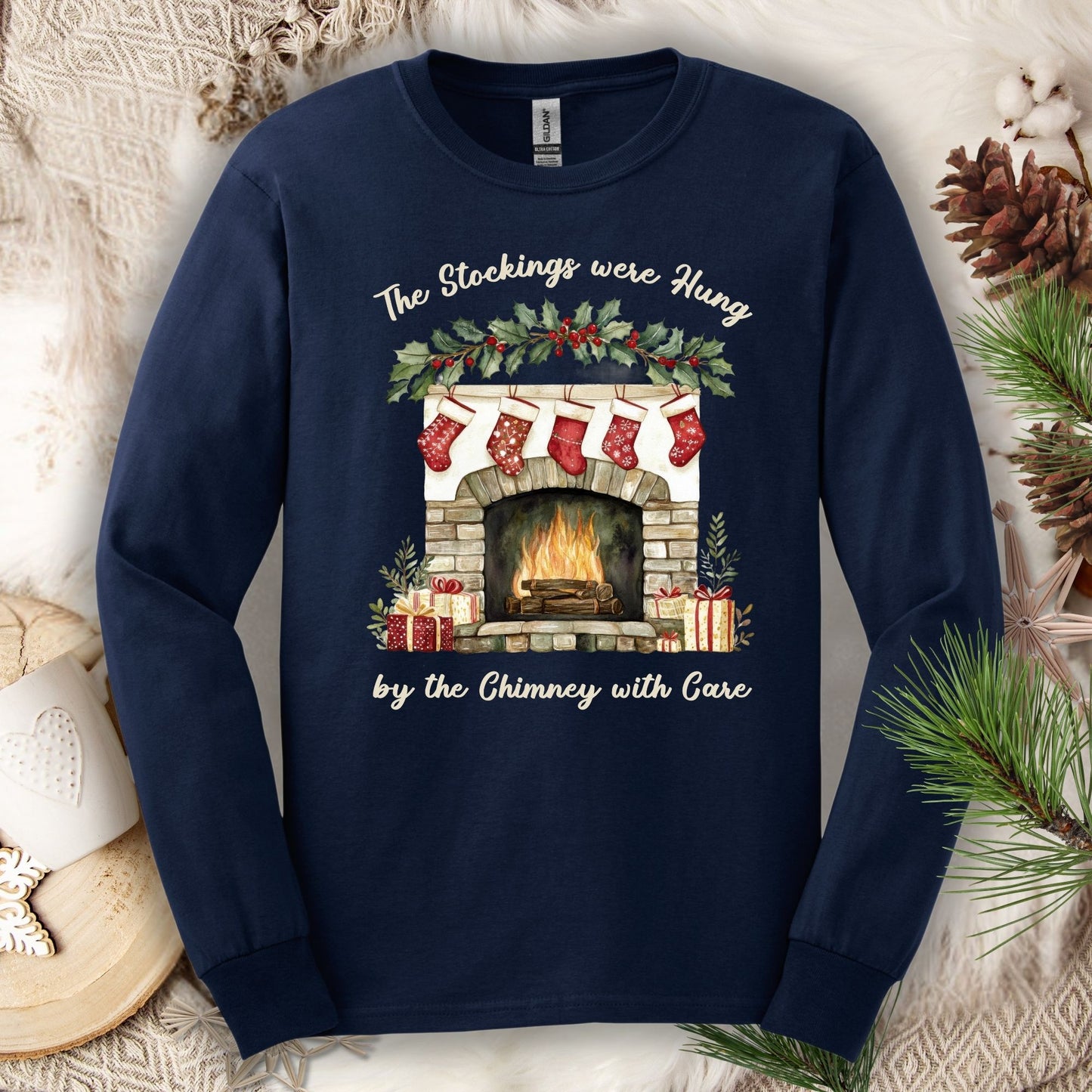 Navy long sleeve tee with a watercolor fireplace, red stockings, holly, and "The Stockings were Hung..." text.