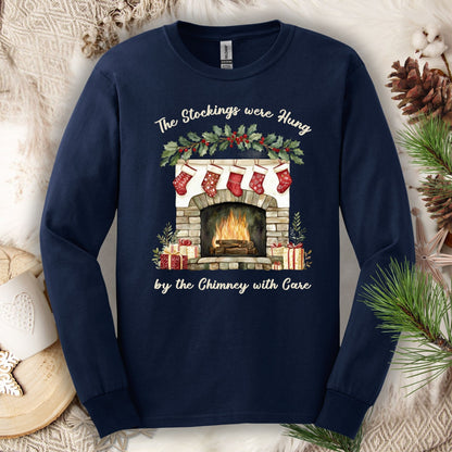Navy long sleeve tee with a watercolor fireplace, red stockings, holly, and "The Stockings were Hung..." text.