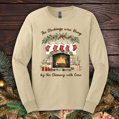 Sand long sleeve tee with a watercolor fireplace, red stockings, holly, and "The Stockings were Hung" text.
