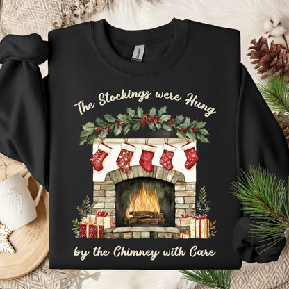 Black Gildan crewneck sweatshirt with a watercolor Christmas fireplace, stockings, and "The Stockings were Hung" text.