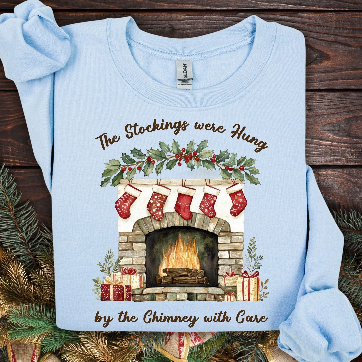 Light blue Gildan crewneck sweatshirt with a watercolor Christmas fireplace, stockings, and holly design.