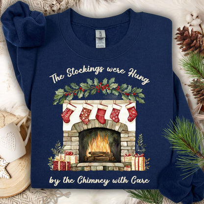 Navy Gildan crewneck sweatshirt with a watercolor Christmas fireplace, red stockings, and "The Stockings were Hung" text.