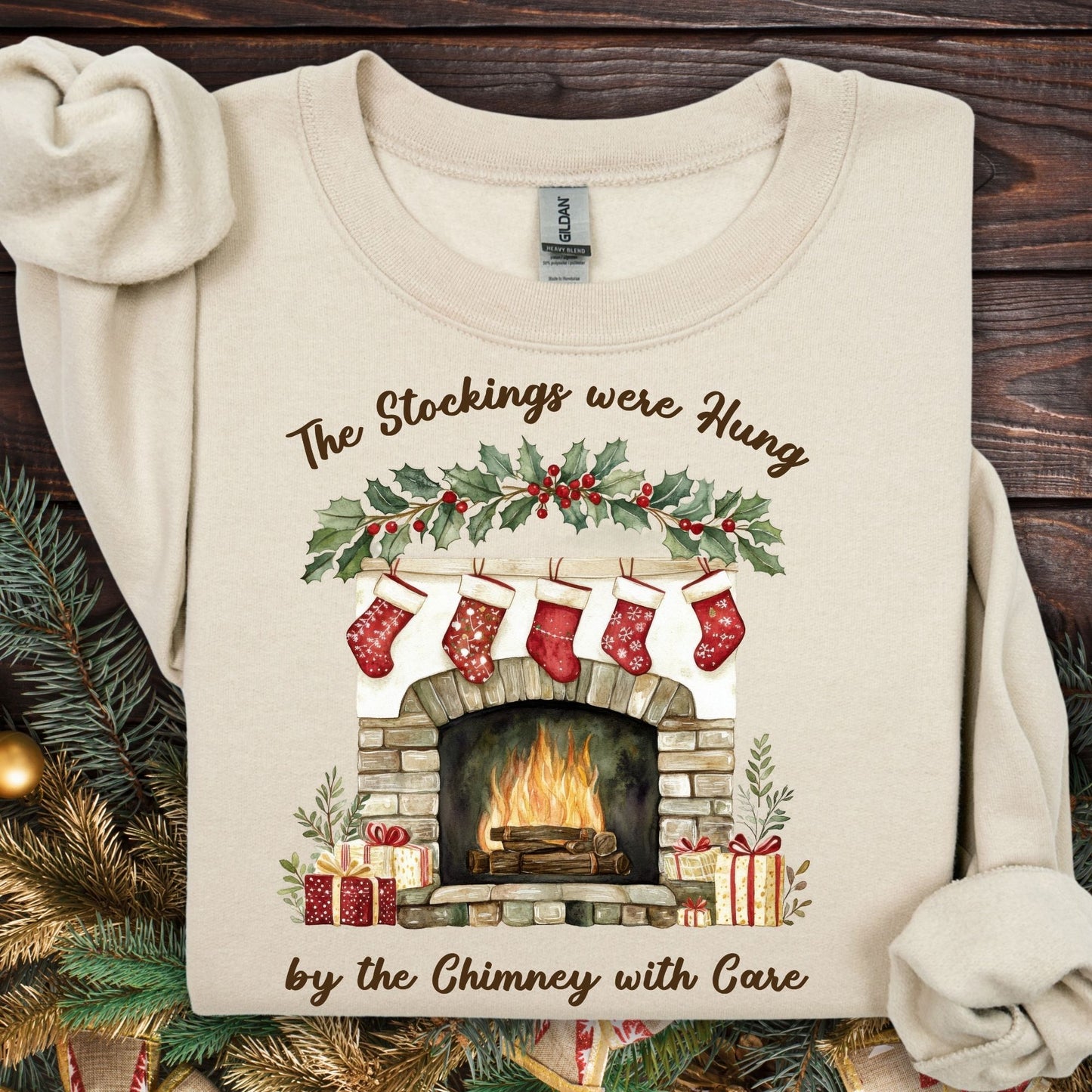 Sand Gildan sweatshirt with watercolor fireplace, red stockings, holly, and "The Stockings were Hung" text.
