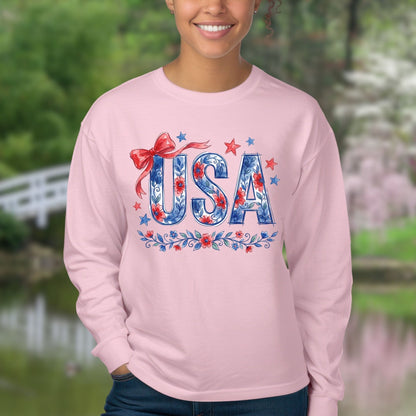 Pink long-sleeve tee with a hand-drawn USA floral flag graphic, red bow, and blue stars.