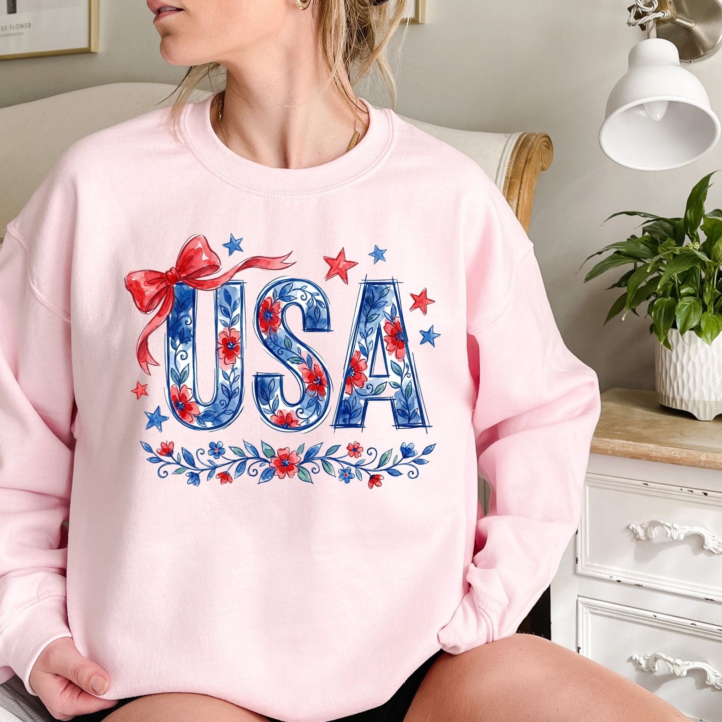 Pink crewneck sweatshirt with "USA" in blue floral print, red bow, and stars.