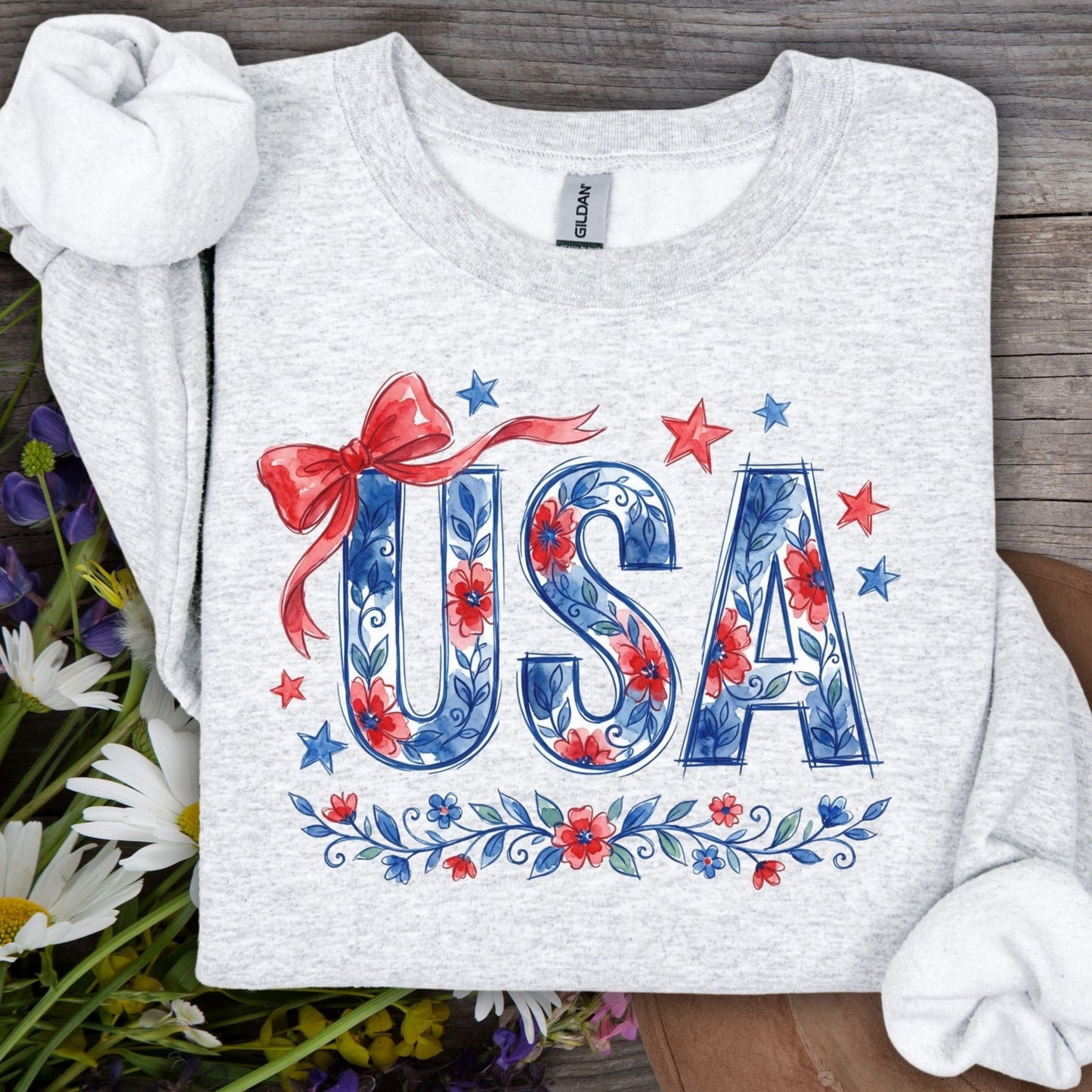 Light gray crewneck sweatshirt with "USA" in blue floral letters, red bow, and stars.