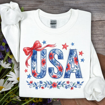White USA Patriotic Floral Sweatshirt with blue floral lettering, red bow, and stars on a wooden background.