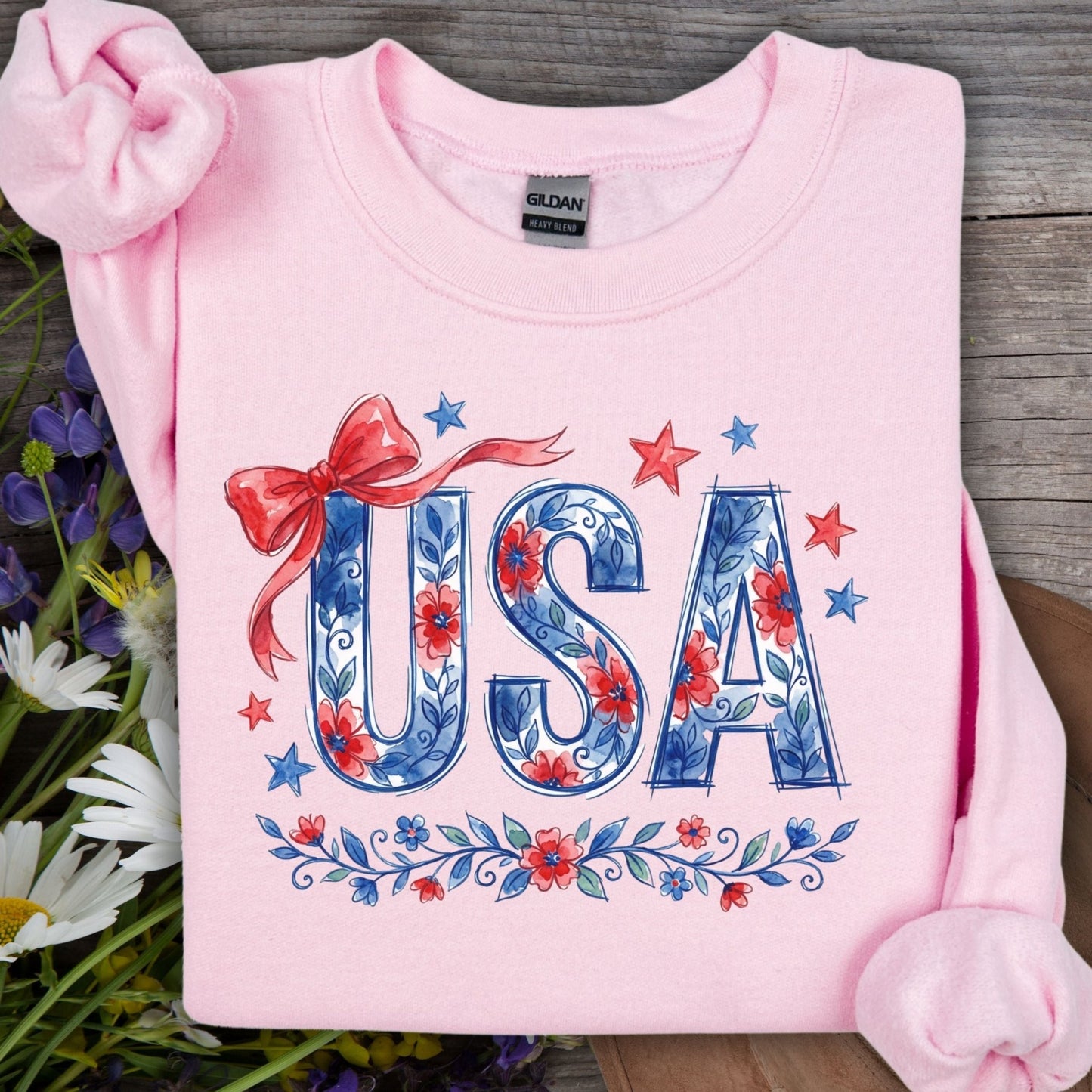 Light pink USA Patriotic Floral Sweatshirt with blue floral lettering, red bow, and stars on wood.