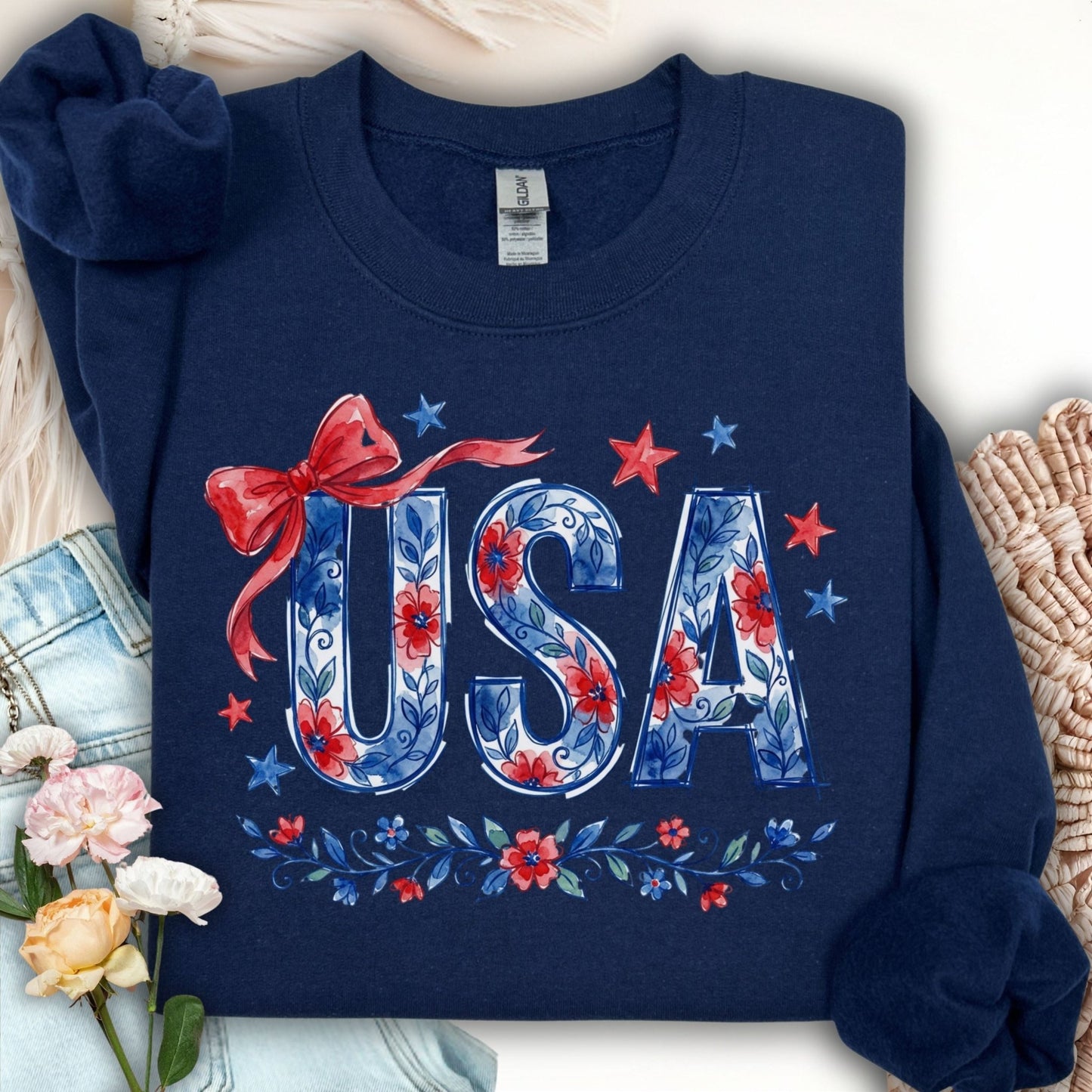 Navy crewneck sweatshirt with "USA" in blue floral print, red bow, and stars.