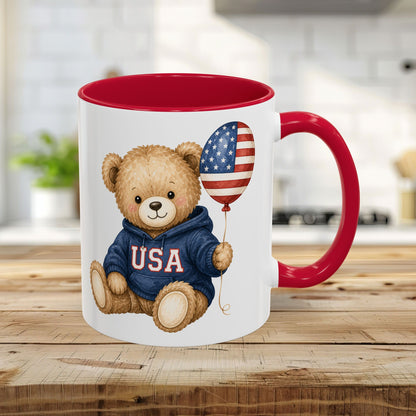 USA teddy bear in blue hoodie holding flag balloon on white ceramic mug with red handle and interior.