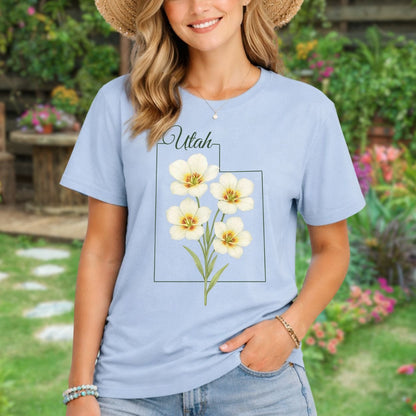 Light blue Utah Sego Lily t-shirt with watercolor floral design, worn by a woman in a straw hat.
