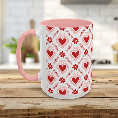 White ceramic mug with pink interior and handle, featuring a repeating red heart and ribbon pattern.