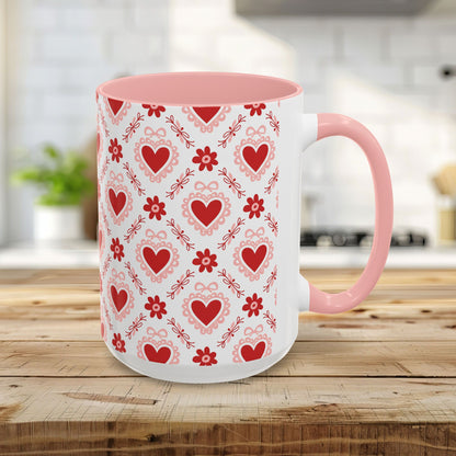 15oz ceramic mug with a pink interior/handle and a repeating red heart, floral, and ribbon pattern.
