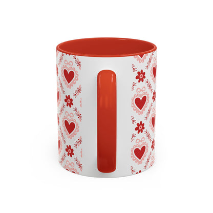 White ceramic mug with red interior and handle, featuring a repeating pattern of red hearts, floral motifs, and bows.