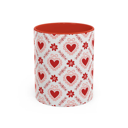 White ceramic mug with red interior and handle, featuring a repeating pattern of red hearts, floral motifs, and bows.