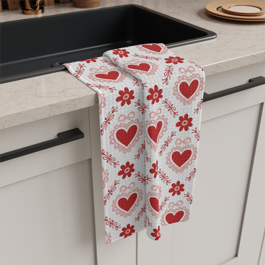 White microfiber tea towel with red hearts, pink carnations, and ribbon pattern, draped over a kitchen counter.