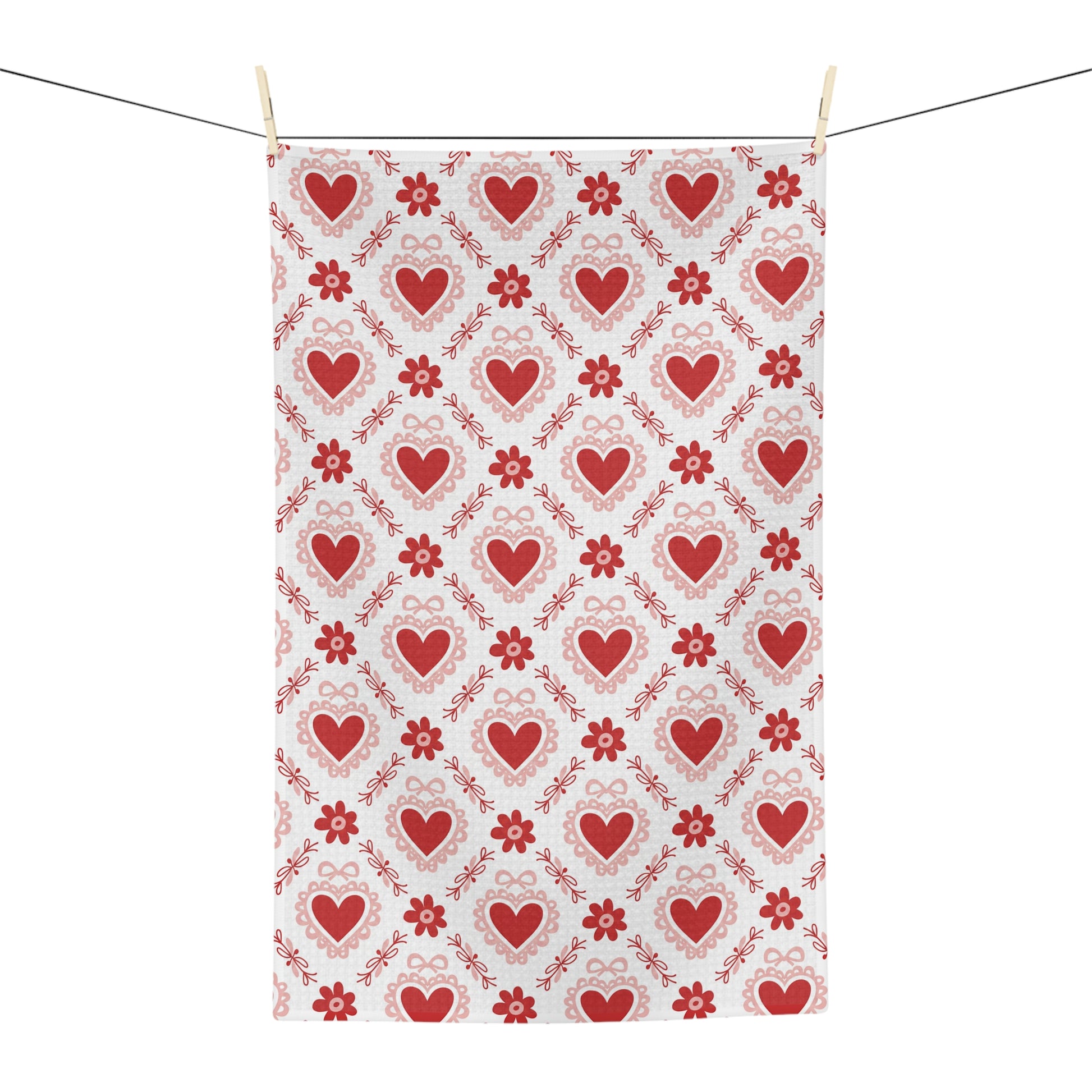 Microfiber tea towel with a repeating pattern of red hearts and small floral motifs, hanging on a clothesline.
