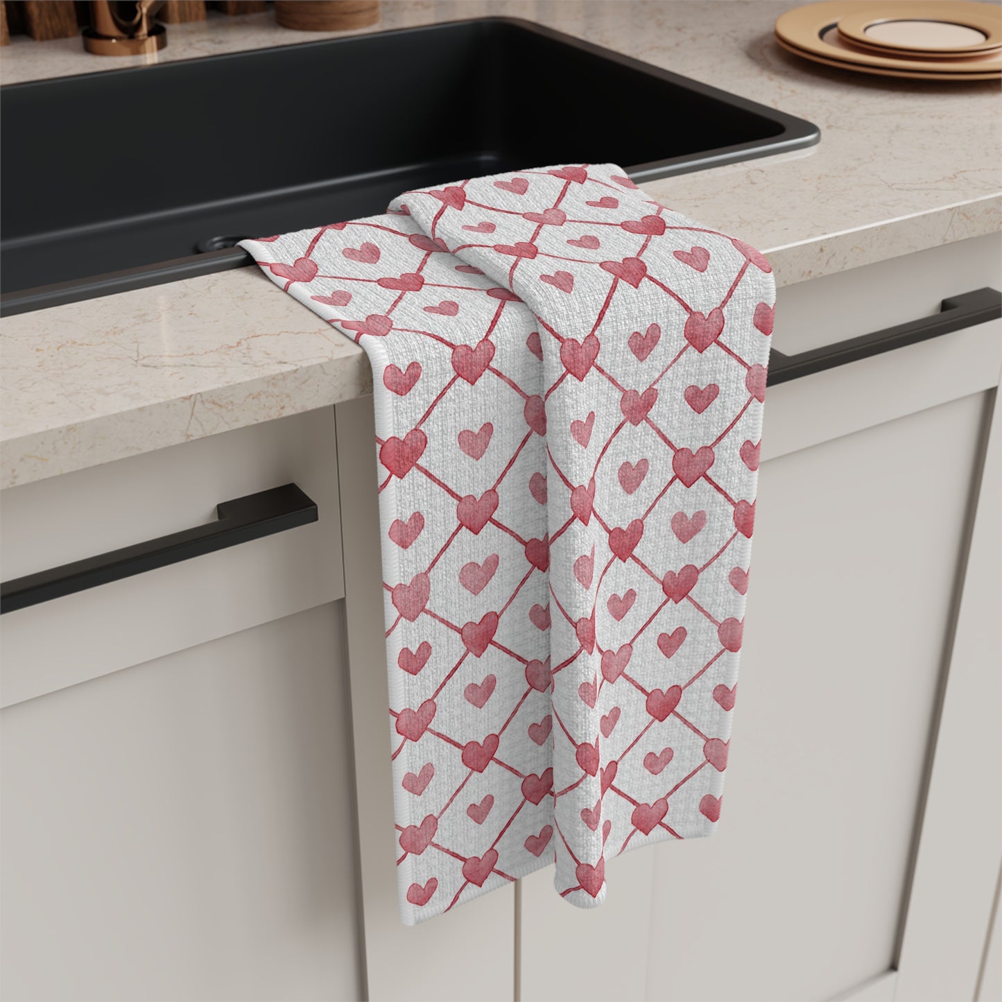 White microfiber tea towel with a red geometric heart pattern draped over a kitchen counter.