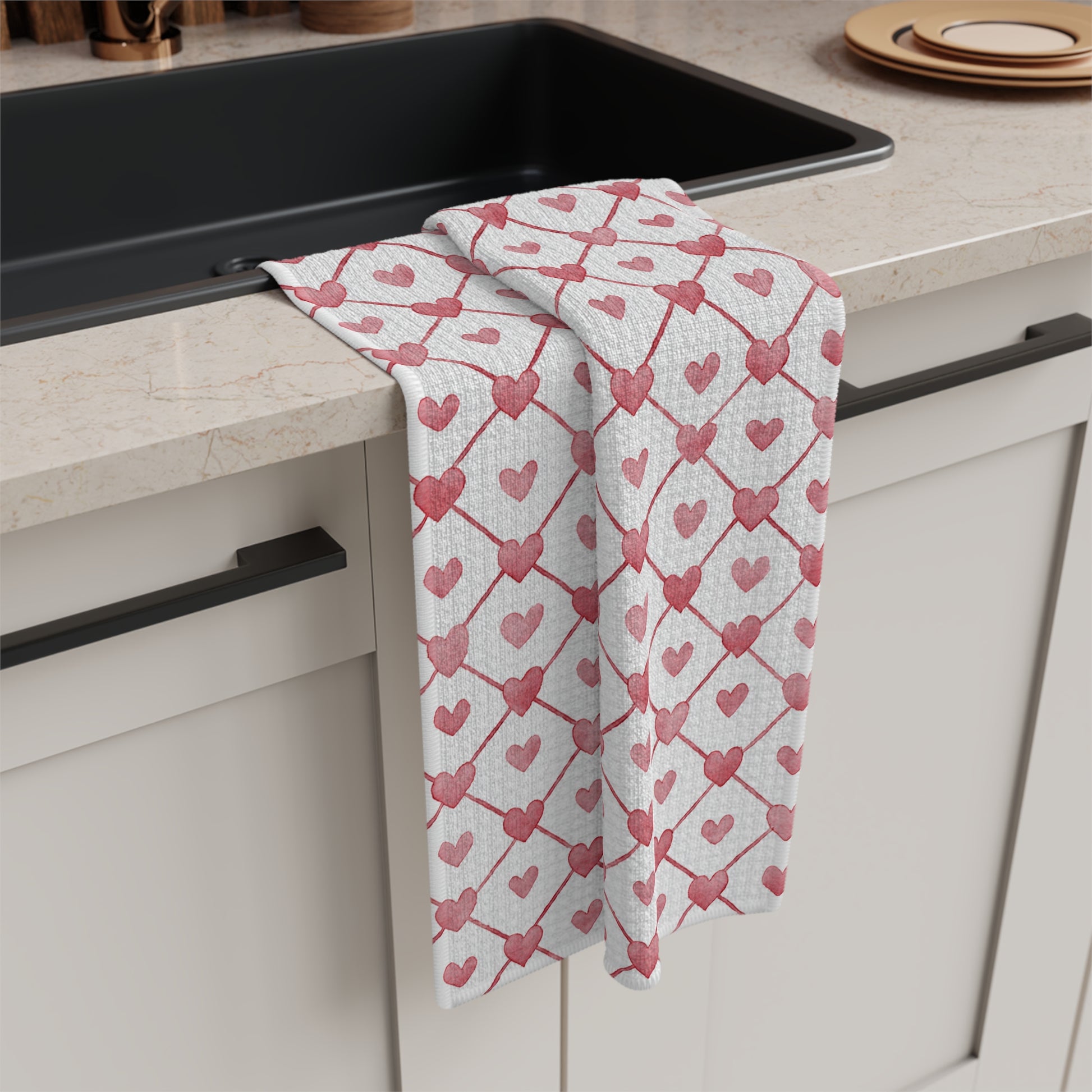 White microfiber tea towel with a red geometric heart pattern draped over a kitchen counter.