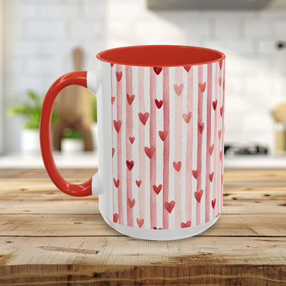 White ceramic mug with watercolor pink stripes and red hearts, red interior and handle, on a wooden table.