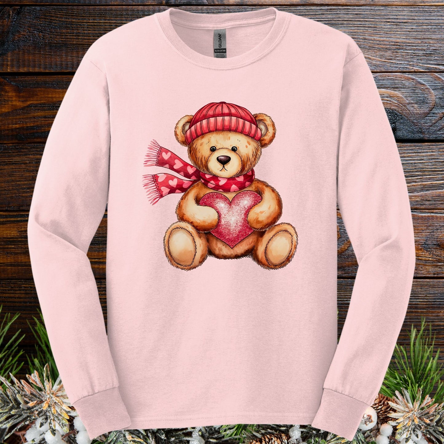 Light pink long sleeve tee with a watercolor teddy bear wearing a red hat and scarf, holding a heart.