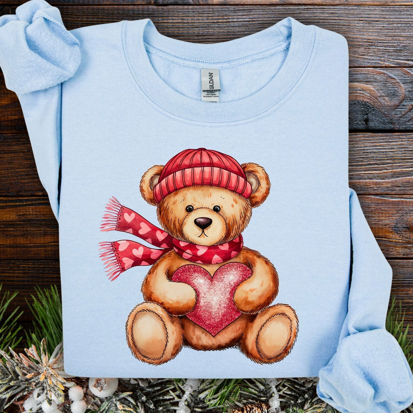 Light blue cotton-polyester sweatshirt with a teddy bear in a red hat and scarf holding a glittery red heart.