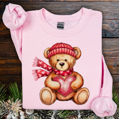 Light pink Gildan sweatshirt with a teddy bear in a red hat and scarf holding a glittery red heart.
