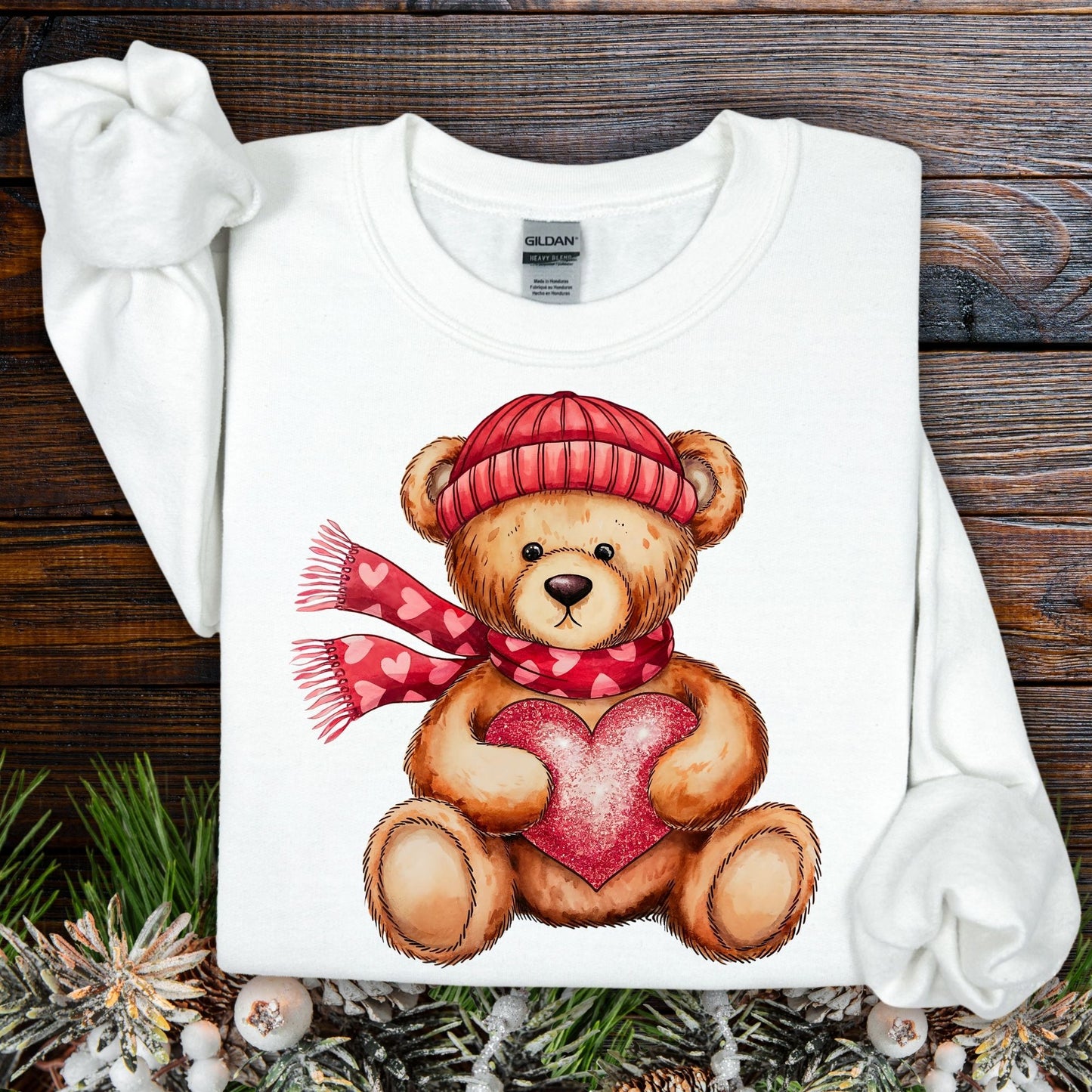 White Gildan heavy blend sweatshirt with a teddy bear in a red hat and scarf holding a glittery heart.