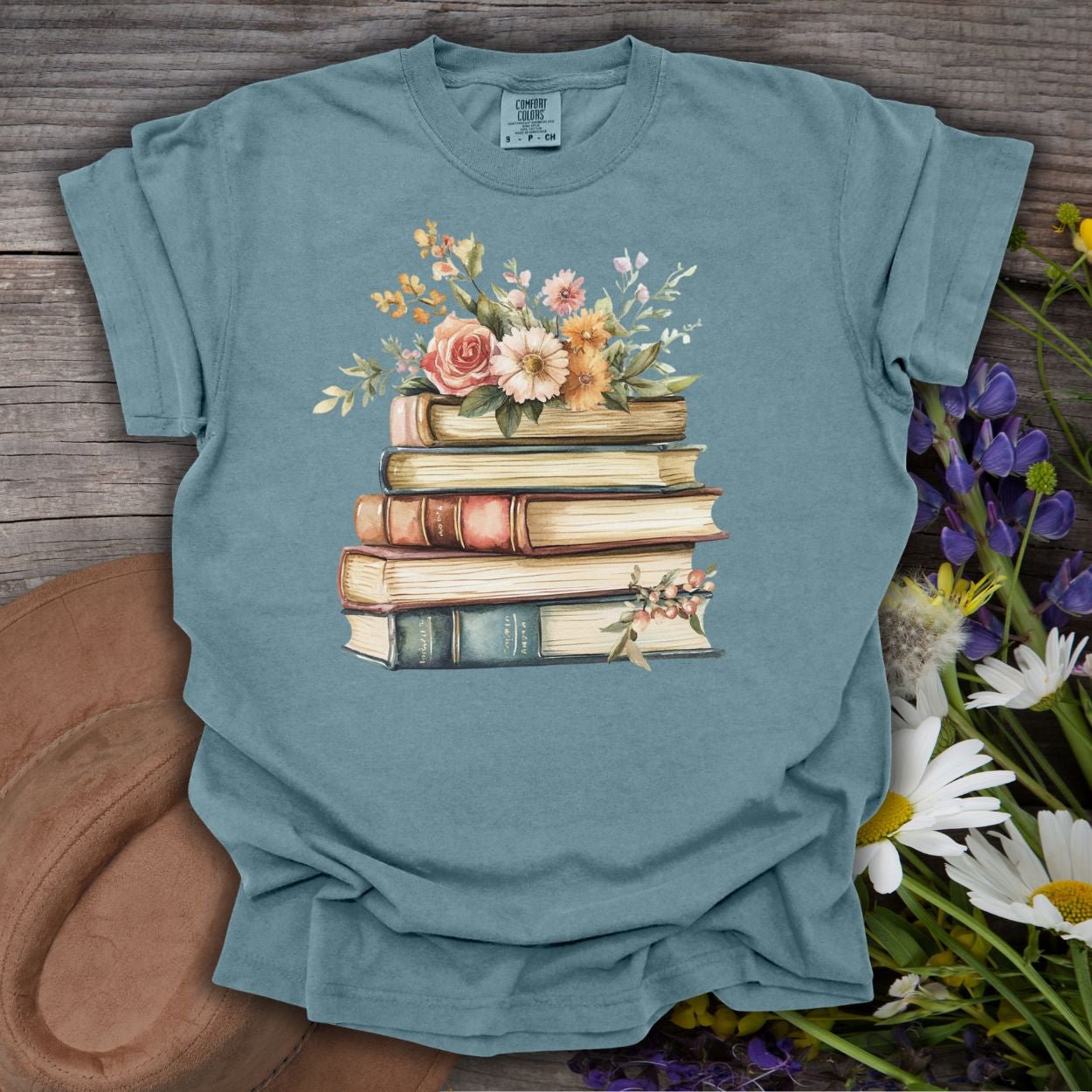 Ice Blue S t-shirt with a vintage books and wildflowers graphic, on a rustic wood background.