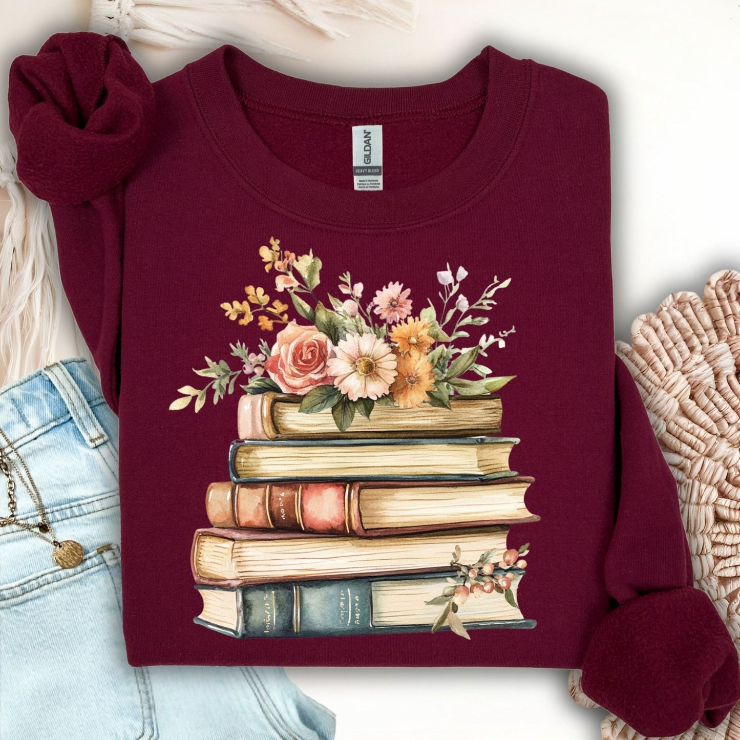 Maroon crewneck sweatshirt with a vintage illustration of stacked books and delicate summer flowers.