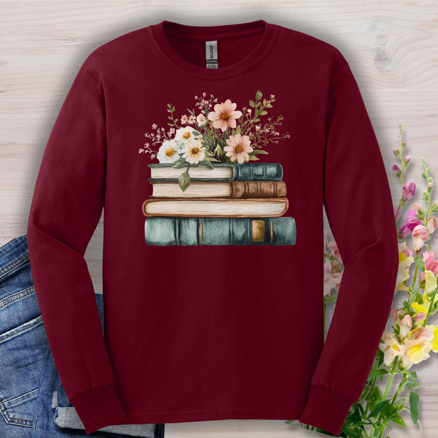 Maroon long-sleeve tee with a vintage stack of books and wildflowers design, soft cotton.