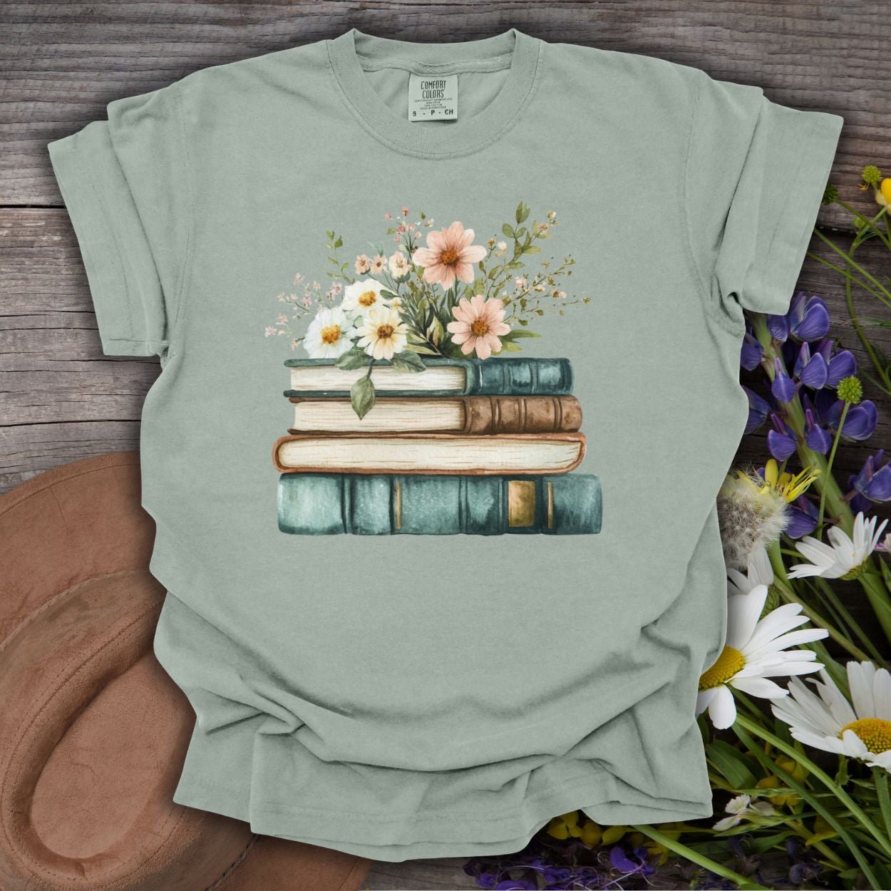 Bay green garment-dyed t-shirt with a stacked books and wildflowers illustration.