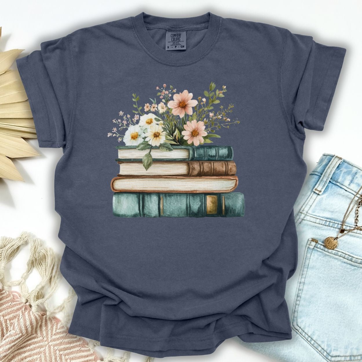 Denim blue garment-dyed cotton t-shirt with a stacked books and wildflowers illustration.
