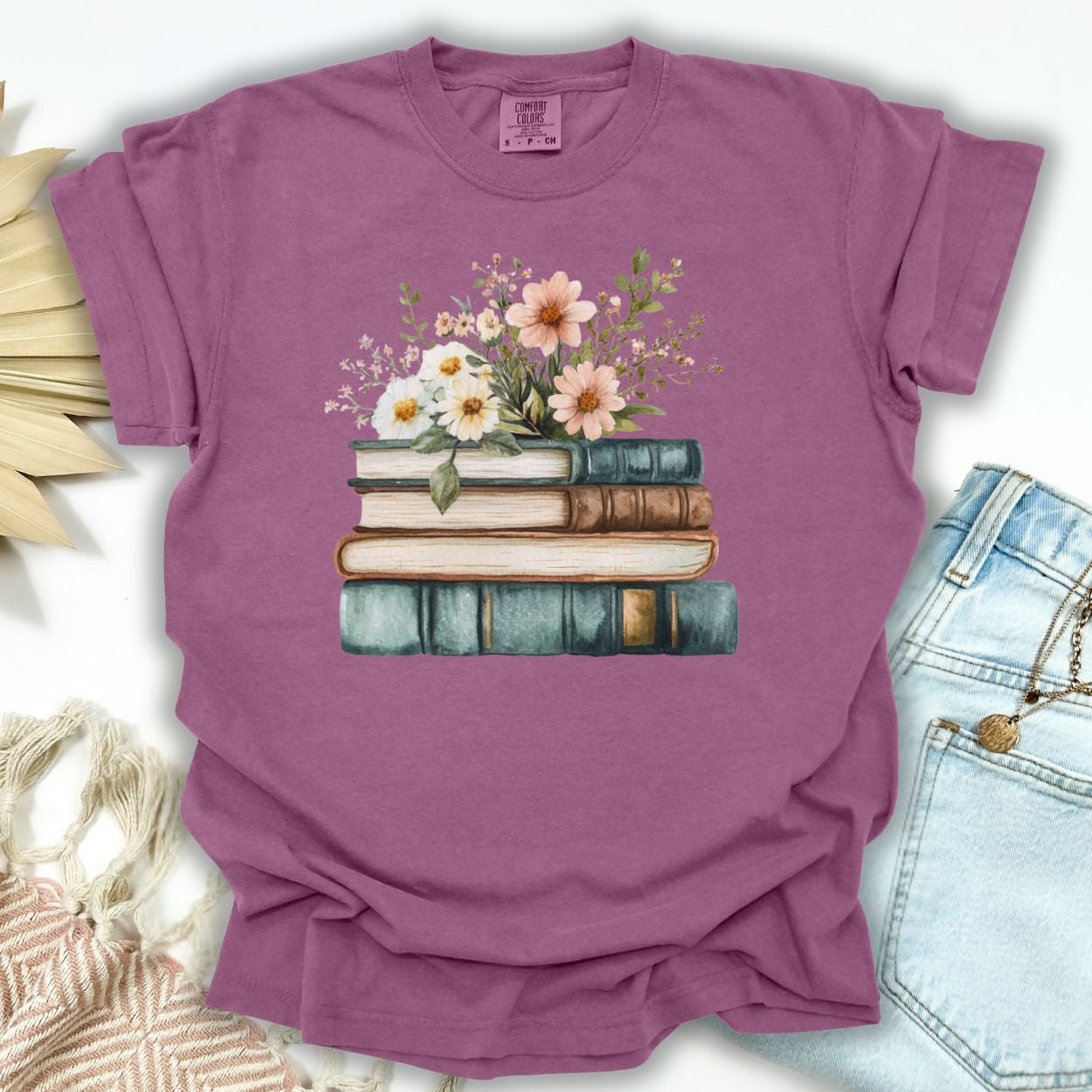 Berry garment-dyed cotton t-shirt with a stack of books and wildflowers illustration.